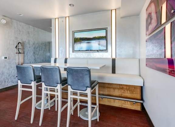 Modern dining nook here at Blue and Lime Apartments with a sleek white table, four high grey chairs, and a white cushioned bench. Nature artwork and warm lighting create a cozy feel.
