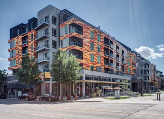 Modern urban Blue and Lime Apartments building with vibrant orange and yellow geometric facade, large windows, balconies, trees, and a clear blue sky.