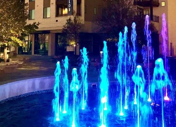 a fountain is lit up at night in front of a building
