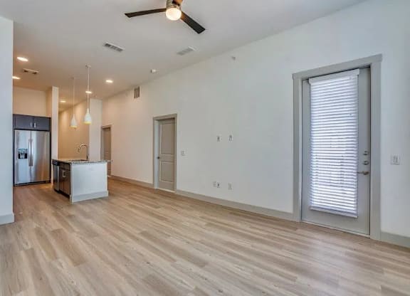 an empty living room with a kitchen and a ceiling fan