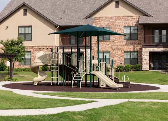 A playground with a green umbrella and a slide.