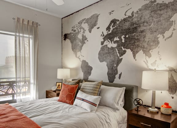 Cozy bedroom here at Proxy 333 Apartments with a world map mural behind the bed. Neutral tones, accented by orange pillows and throw on the bed, create a warm and inviting atmosphere.