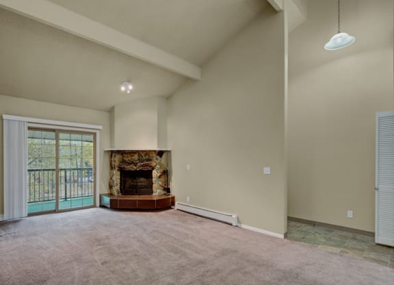 Spacious living room here at Ptarmigan Meadows with high ceilings, featuring a stone fireplace and large sliding glass doors to a balcony. Neutral tones create a calm atmosphere.