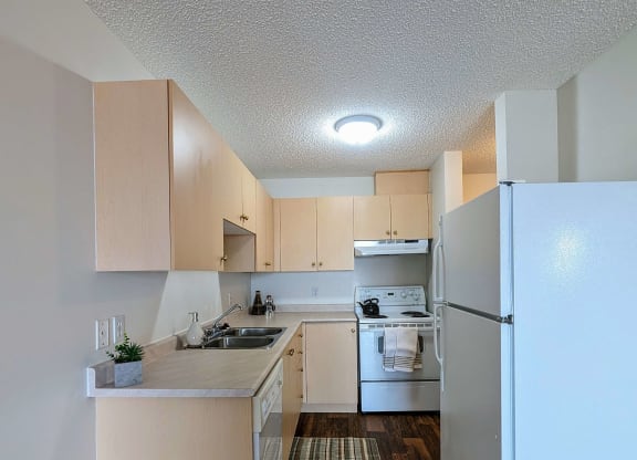 an empty kitchen with white appliances and wooden floors