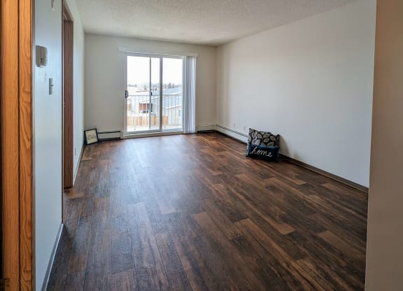 an empty living room with wood flooring and a door to a balcony