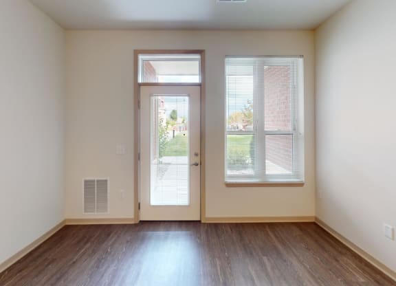 a living room with white walls and wood floors and a door to a balcony
