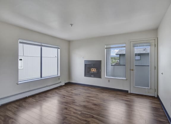 Empty living room here at Silver Ridge Apartments with light wood flooring, white walls, and a modern fireplace. Large windows and a glass door provide natural light. Cozy and minimalistic.