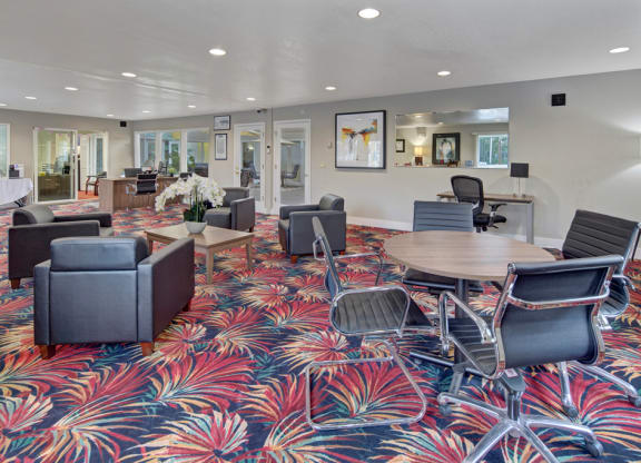 Modern office lobby here at The Club at Eagle Pointe Apartments with vibrant red and blue floral carpet, featuring gray armchairs, wood tables with orchids, and sleek black office chairs. Bright and welcoming atmosphere.