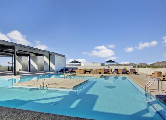 a large swimming pool with lounge chairs and umbrellas on a sunny day