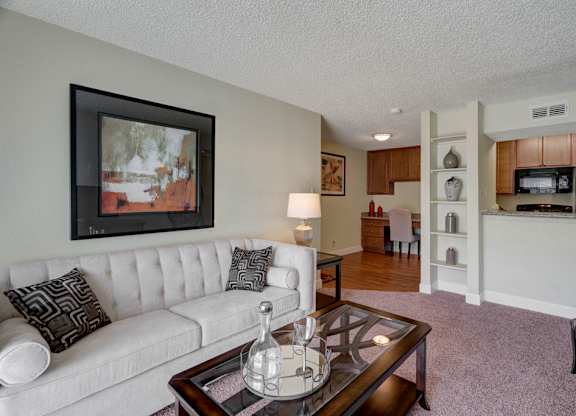 A cozy living area at Acacia Park featuring soft carpeting, a comfortable seating layout, warm accent lighting, and an open connection to the kitchen and dining space for an inviting, easy-to-live-in feel.