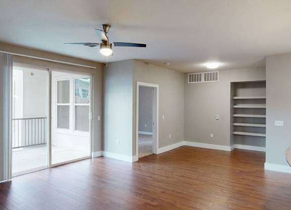 A spacious open living area here at BRIO at Firewheel with wood-style flooring, ceiling fan, sliding glass doors to a balcony, built-in shelving, and an open layout connected to the kitchen.