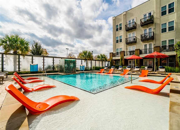A pool surrounded by orange chairs and a building in the background.