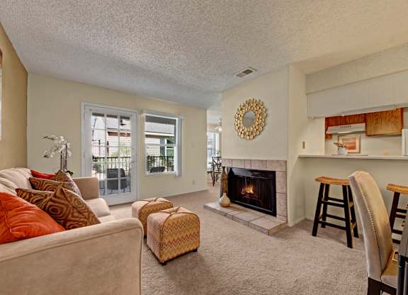 A warm, inviting living room here at Cypress Pointe with soft beige carpet, neutral walls, and a cozy fireplace serving as a central feature. An open layout connects to the kitchen with a breakfast bar and seating, while glass doors bring in natural light and provide access to a private patio.