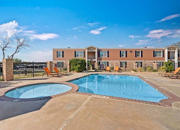 A refreshing outdoor swimming pool here at Golden Crest with clear blue water, a spacious concrete deck, and surrounding lounge chairs, featuring a separate shallow pool area and a fenced courtyard setting under bright, sunny skies.