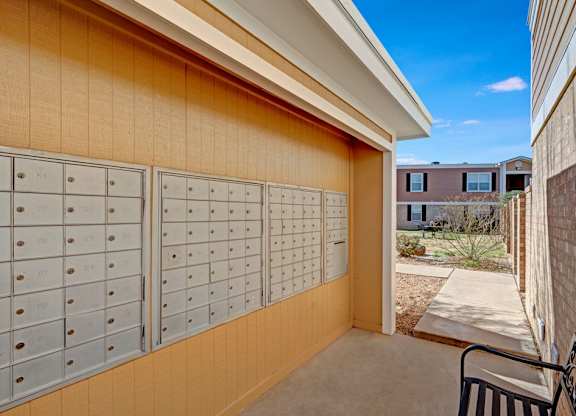 A covered community mailbox area here at Golden Crest with neatly organized mailboxes, neutral-toned siding, and a shaded walkway that leads into the landscaped courtyard, offering a convenient and accessible mail pickup space.