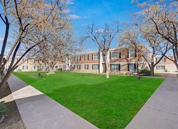 A peaceful outdoor courtyard here at Golden Crest with a wide grassy lawn, mature trees, and smooth walking paths, surrounded by apartment buildings and picnic tables that create a calm, community-friendly setting.