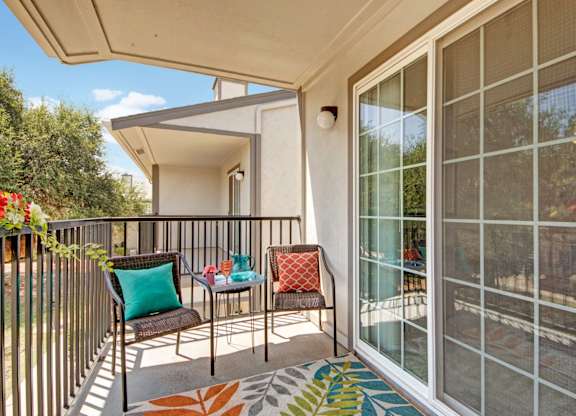 A private outdoor balcony here at High Plains with a small seating area, decorative pillows, and a sliding glass door, offering fresh air, natural light, and a comfortable space for relaxing or enjoying the view.