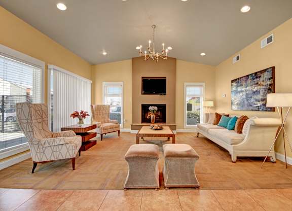 A spacious community lounge here at High Plains with comfortable seating, warm neutral tones, a central fireplace with a mounted TV, and large windows that bring in natural light, creating an inviting space for relaxing or gathering with others.