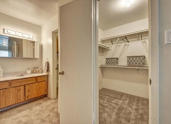 A convenient bathroom and closet area here at High Plains with a wooden vanity and light countertop, a mirrored medicine cabinet with overhead lighting, and an adjacent walk-in closet with shelving, offering a functional and organized layout.
