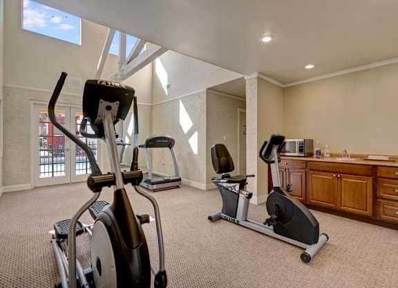 A well-equipped fitness center here at Las Colinas with cardio machines, including treadmills and stationary bikes, set on plush carpeting. Large windows and bright lighting create an open, energizing space, with a convenient counter area adding comfort for residents during workouts.