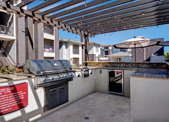 A BBQ grill is on a patio with a sign that says "Kitchen Rules".