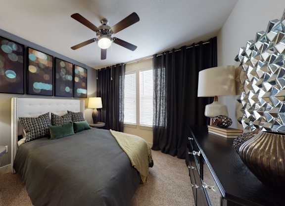 A bedroom with a bed, a ceiling fan, and a side table with a lamp.
