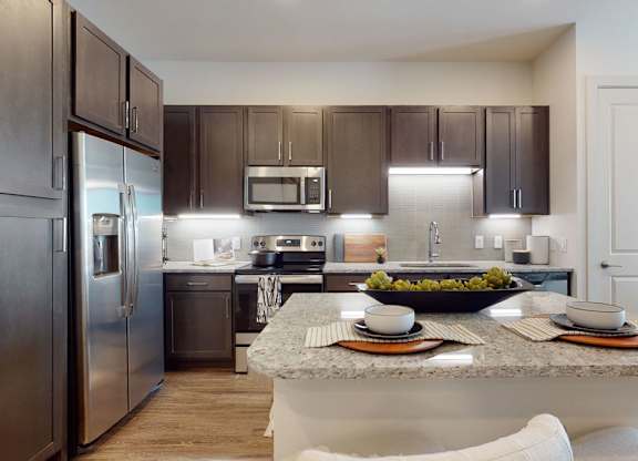 A modern kitchen here at Magnolia on the Green with dark wood cabinets, granite countertops, stainless steel appliances, a center island with seating, and bright under-cabinet lighting for a clean, upscale feel.