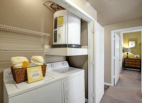 A convenient laundry area here at Palms at Briarwood featuring a stacked washer and dryer with built-in shelving, neutral walls, and easy access from the hallway, offering a practical and organized space for everyday laundry needs within the apartment home.