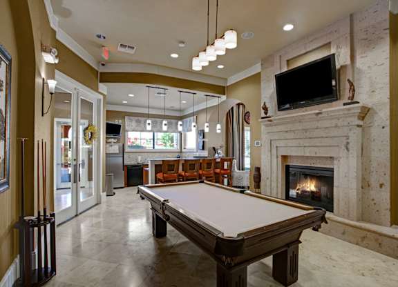 A stylish resident lounge here at Palms at Briarwood featuring a pool table, stone fireplace, mounted television, and bar seating, with pendant lighting, polished floors, and an open layout creating a welcoming space for relaxing, socializing, and entertaining guests.