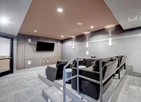 A media room here at Sorrel Fairview with tiered theater seating, dark gray lounge chairs, wall-mounted TV, wood accent wall, and soft recessed lighting for a cozy viewing space.