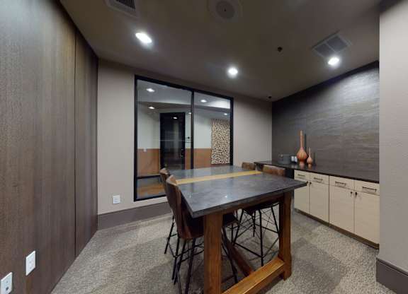 A work lounge here at Sorrel Fairview with a tall dark wood table, brown leather stools, stone-look tabletop, light wood cabinets, and a sleek accent wall, creating a modern, quiet meeting space.