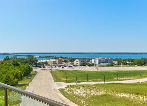 A balcony view here at Sorrel Fairview overlooking a wide green lawn, curving road, and bright blue lake in the distance under clear sunny skies.
