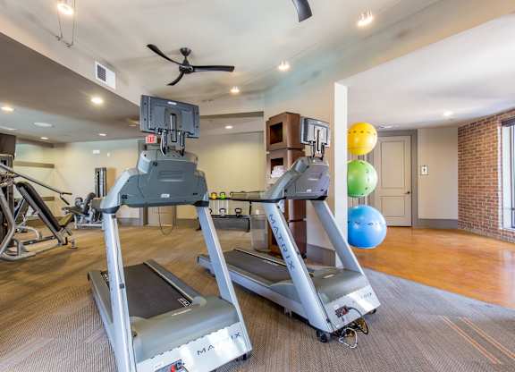 A fitness center here at Sorrel Fairview with modern treadmills, strength machines, free weights, colorful exercise balls, track lighting, and warm wood-tone floors in a bright, spacious workout room.