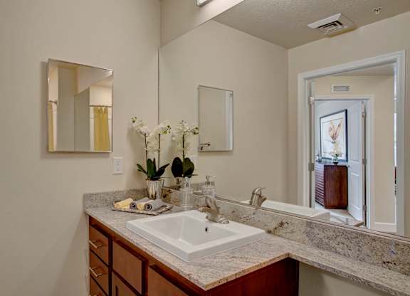 A bathroom with a sink, mirror, and a vase of flowers.