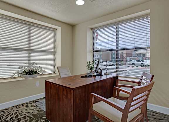 A room with a desk and a chair in front of a window with blinds.