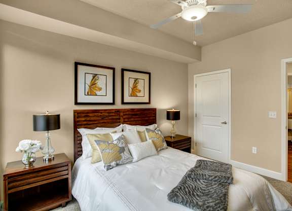 A bedroom with a bed, two lamps, and two framed pictures on the wall.