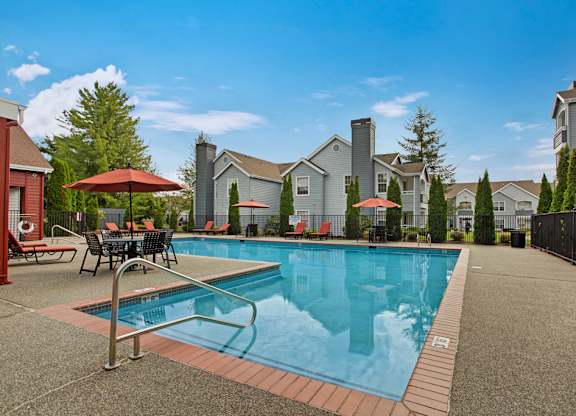 A swimming pool surrounded by a patio with chairs and umbrellas.
