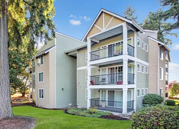 A large apartment building with a balcony and a tree in front.