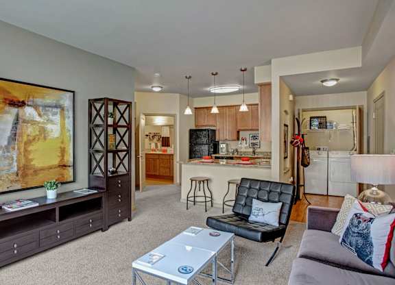 A modern open-concept living room here at Riverside 9 featuring cozy seating, stylish artwork, a breakfast bar with pendant lighting, and an in-home washer and dryer for added convenience.