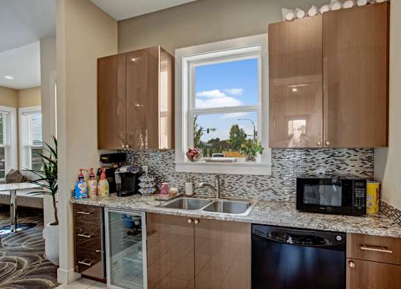 A convenient community kitchen here at Riverside 9 with modern cabinets, granite countertops, mosaic backsplash, sink, and beverage appliances in a bright, welcoming space.