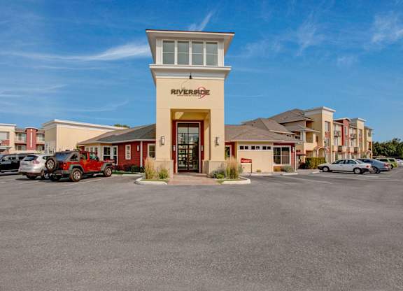 An exterior view here at Riverside 9 highlighting the welcoming leasing office entrance with tall windows, modern architecture, and convenient resident and guest parking.
