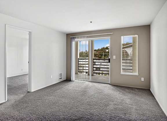 A room with a carpeted floor and a view of a balcony through a glass door.