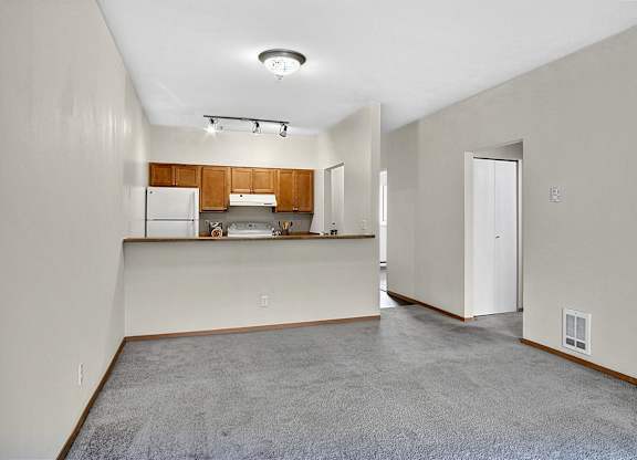 Empty room with a kitchen area in the background.