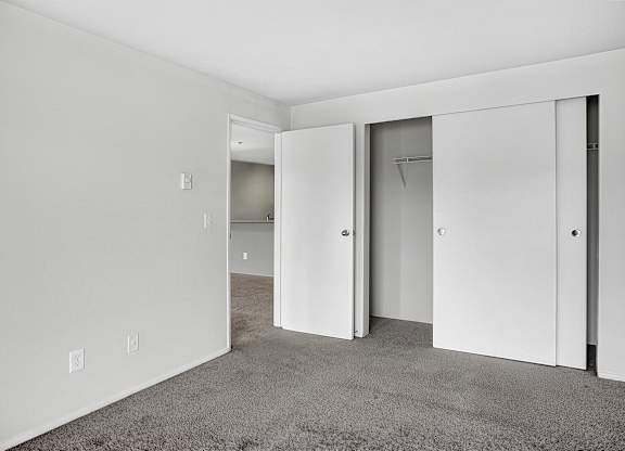 A room with white walls and a carpeted floor with three open doors.