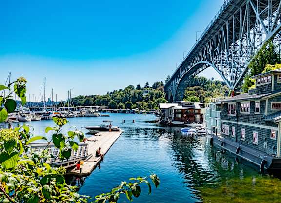 A bridge spans across a calm body of water with houses on the right and boats in the distance.