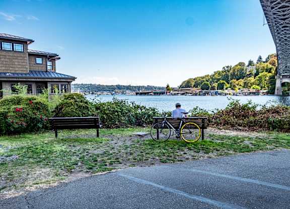 A person is riding a bicycle on a path near a bench.