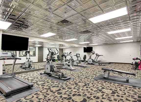 A gym with treadmills, exercise bikes, and a television.