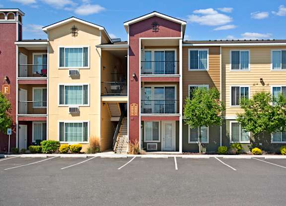 A colorful apartment building exterior here at The Vintage with warm yellow and red siding, private balconies, and large windows. Landscaped greenery and nearby parking create a welcoming community setting.