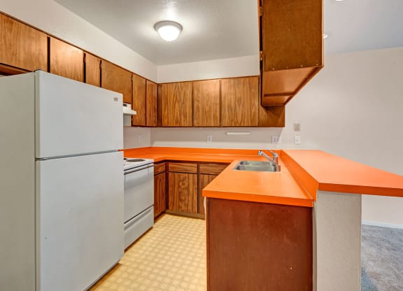 Kitchen with wood cabinets and bright orange countertops. Features a white fridge, stove, and stainless steel sink, conveying a retro aesthetic. Arbor Pointe Apartments.