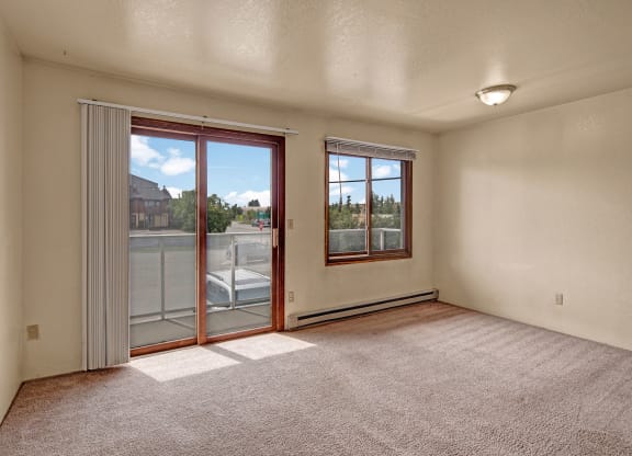 Empty living room with beige carpet and cream walls, featuring a large sliding glass door and window allowing natural light and view of the outside, creating an airy feel. Arbor Pointe Apartments.